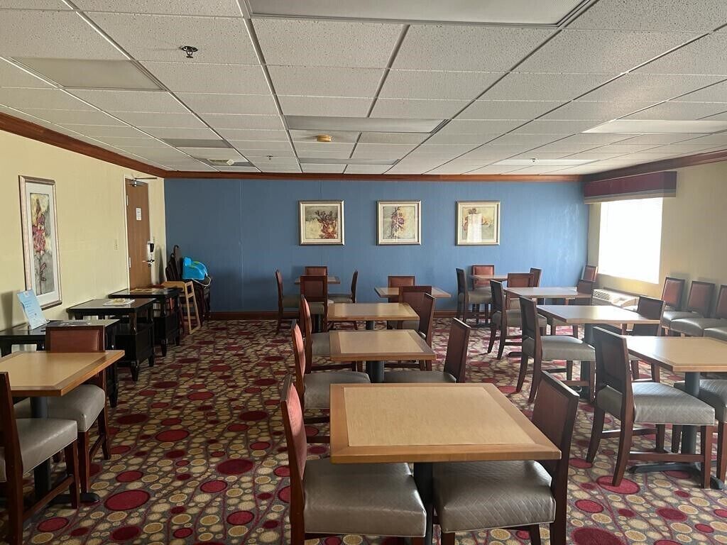 A dining area with tables and chairs, a patterned carpet, and framed artwork on the walls.
