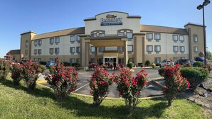 A Baymont Inn & Suites with a central entrance, multiple floors, and a parking lot with red flowering bushes. - Baymont by Wyndham Evansville North/Haubstadt (Haubstadt)