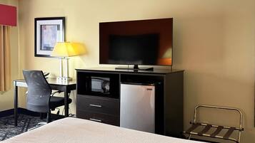 A hotel room with a bed, a desk with a lamp, a television, a refrigerator, and a chair.