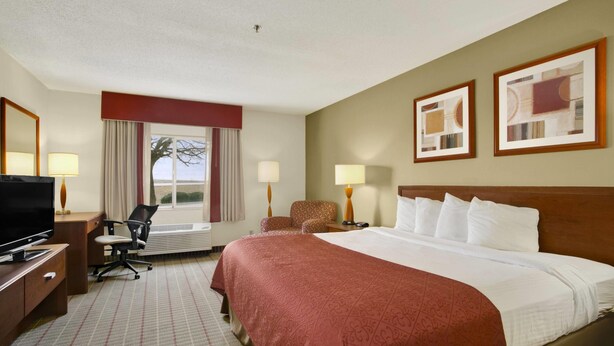 A hotel room with a large bed, a desk with a TV, a chair, and two lamps. - Baymont by Wyndham Evansville North/Haubstadt (Haubstadt)