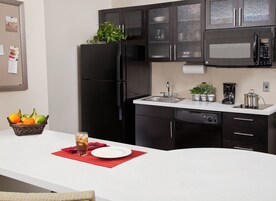 Una cocina moderna con un refrigerador negro, un microondas, un lavabo y un comedor con un plato, un vaso y una cesta de fruta.