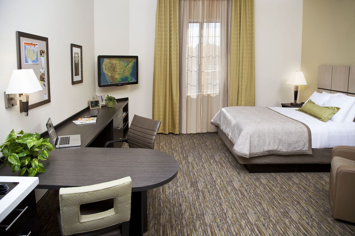 A hotel room with a bed, desk, chair, lamp, and a map on the wall.