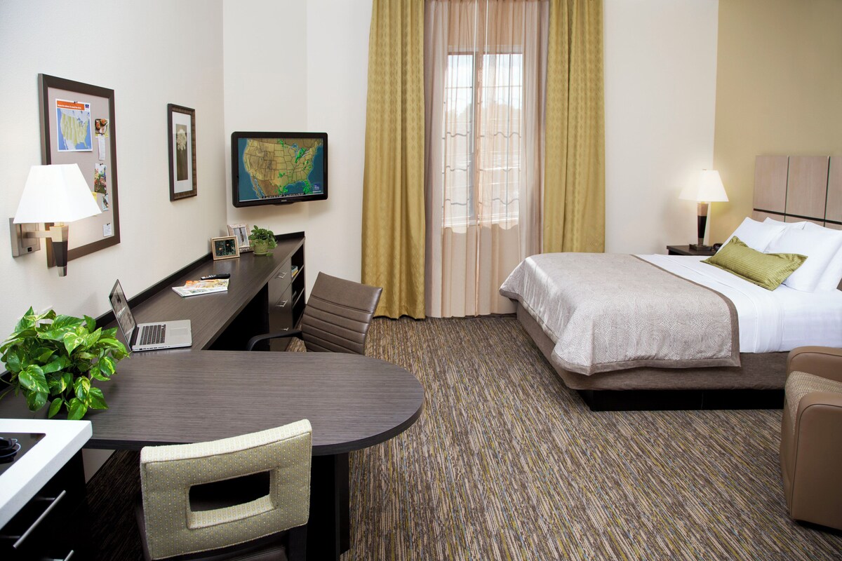 Habitación de hotel con cama, escritorio, silla, lámpara y un mapa en la pared.