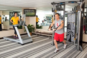Un gimnasio con cintas de correr, una máquina de pesas y un espejo que refleja el interior.