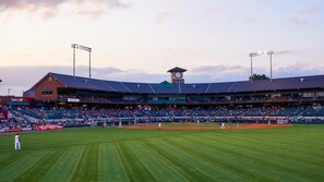 Un estadio de béisbol con una torre de reloj, asientos en niveles y un campo bien cuidado.