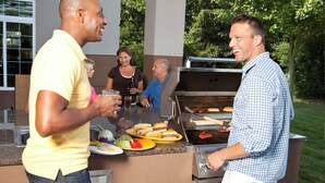 Een buitenbarbecue met een grill, eten en mensen die gezellig samenkomen.