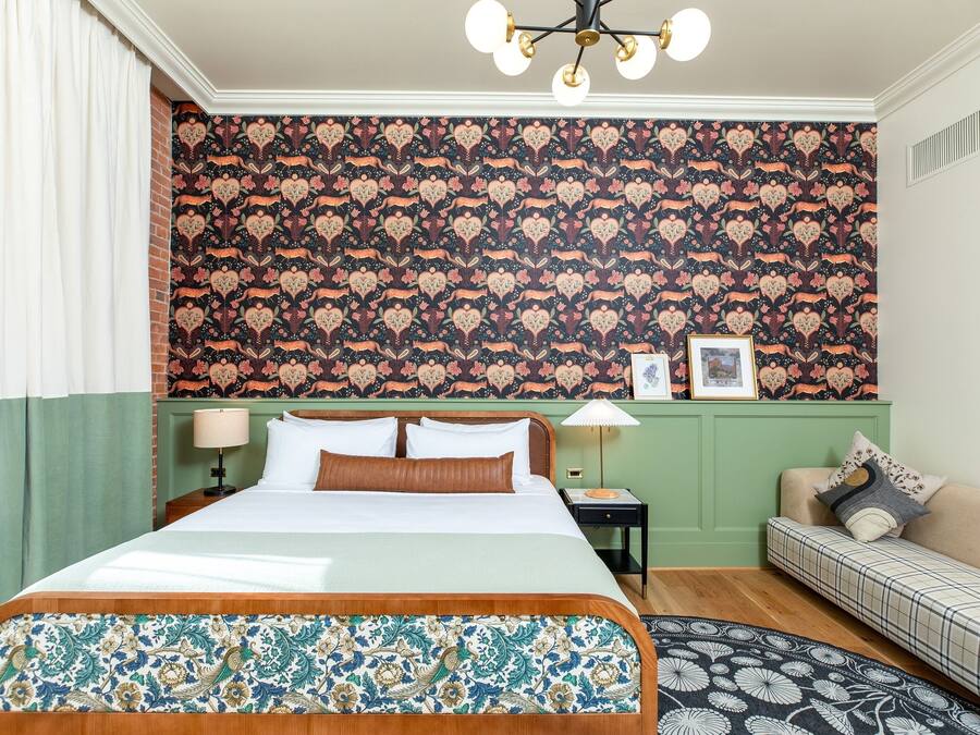 Una habitación de hotel con una cama grande, un muro decorado en verde, un sofá estampado y una araña.