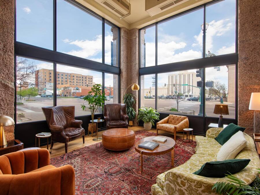 A spacious lobby with large windows, leather armchairs, a patterned rug, and a variety of seating options.
