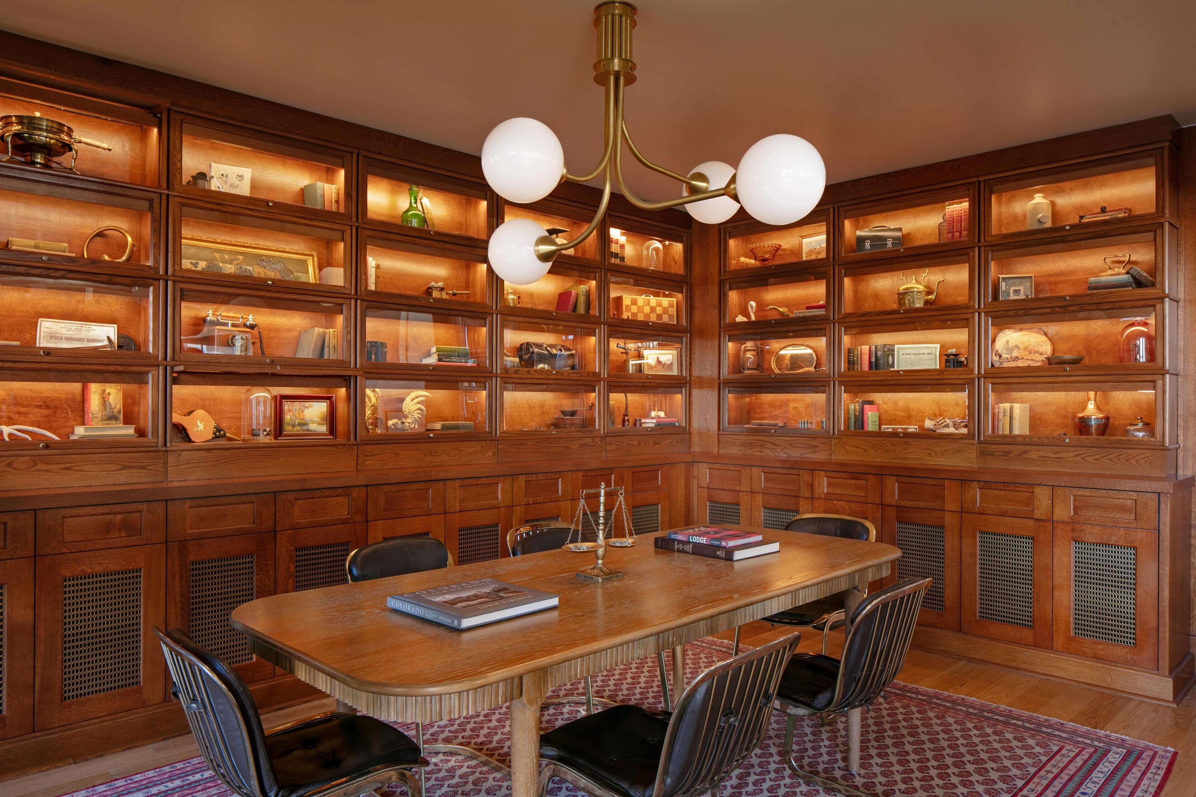 Uma biblioteca com estantes de madeira, uma mesa central e cadeiras.