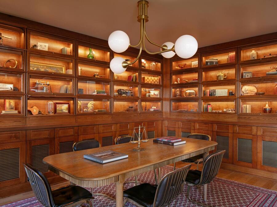 Uma biblioteca com estantes de madeira, uma mesa central e cadeiras.