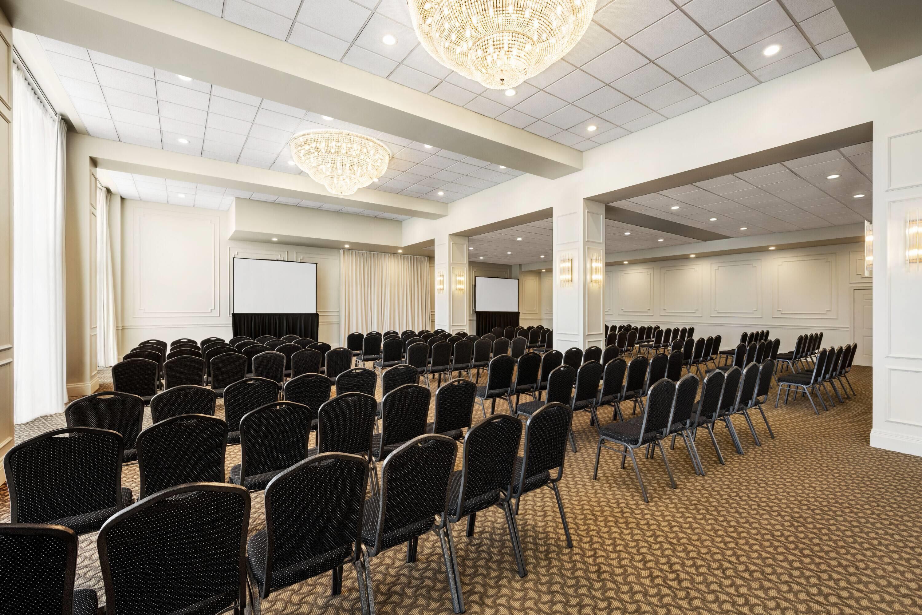 Un salón de conferencias con filas de sillas, una pantalla de proyector y una lámpara de araña grande.