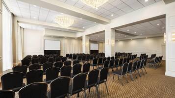 Un salón de conferencias con filas de sillas, una pantalla de proyector y una lámpara de araña grande.