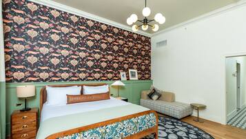 Een slaapkamer met een groot bed, een groene muur, een vloerkleed met patroon en een kroonluchter.