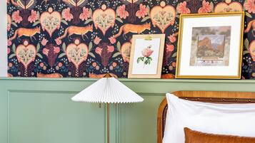 A bedroom with a patterned wallpaper, a framed picture, a bedside lamp, and a bed with a white and brown pillow.