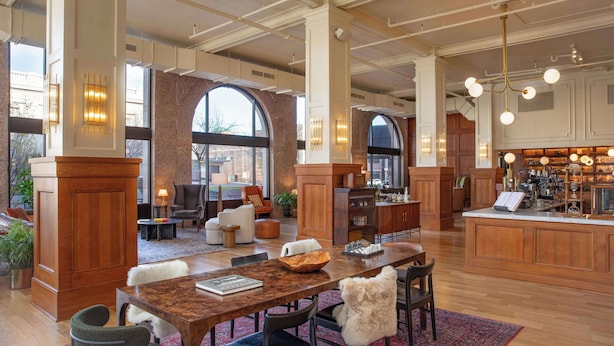 A spacious hotel lobby with a large wooden reception desk, comfortable seating areas, and a view of the city through large windows.