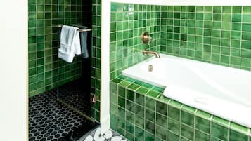 A bathroom with green tiled walls, a white bathtub, and a black and white hexagonal floor pattern.