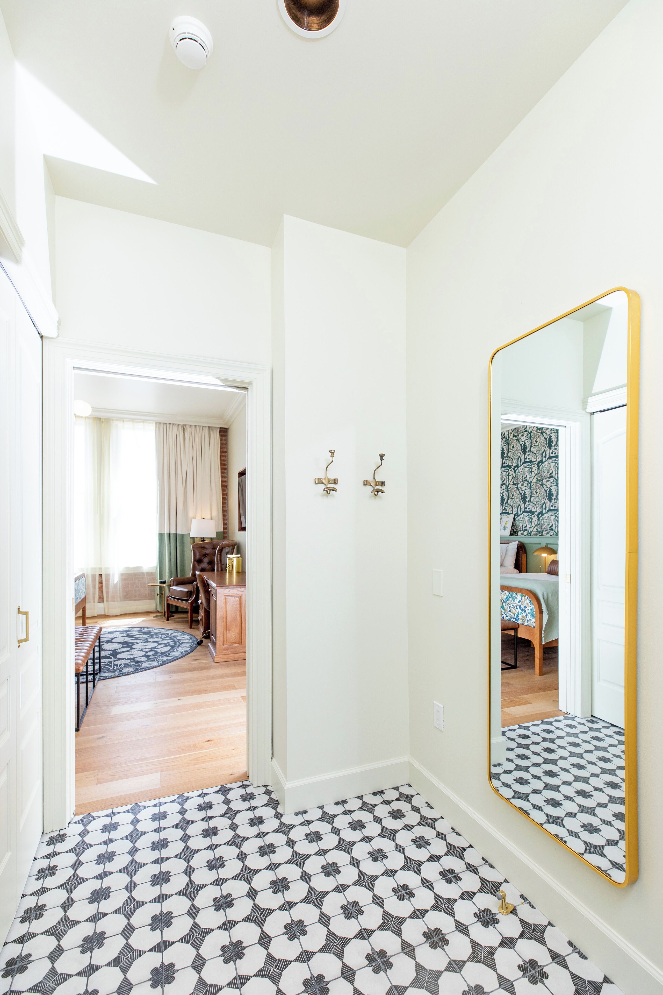Un couloir doté d’un sol à motifs, d’un grand miroir et d’une porte donnant sur une pièce où se trouvent un tapis à motifs et des meubles.