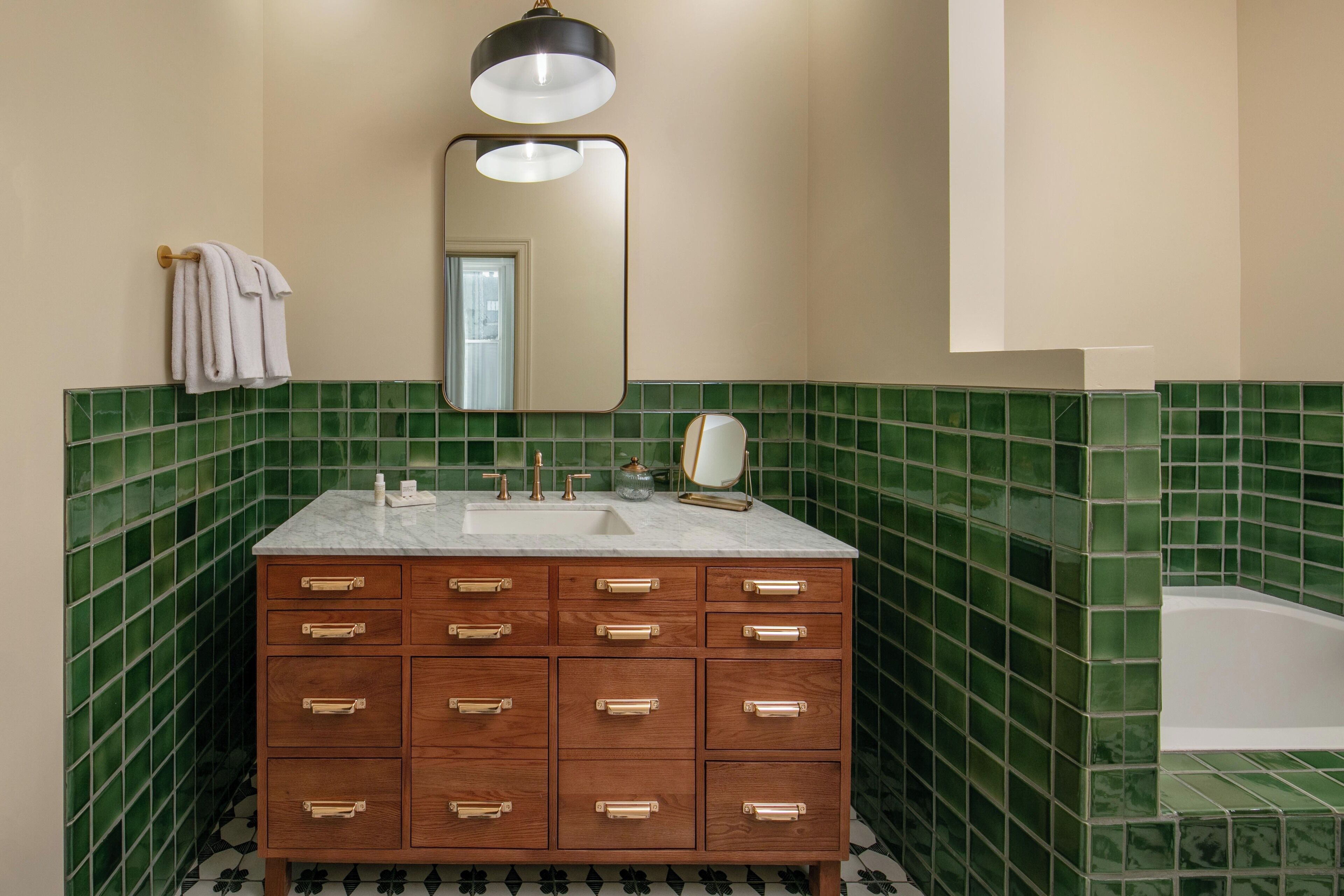 A bathroom with a wooden vanity, green tiled walls, a white sink, and a mirror.