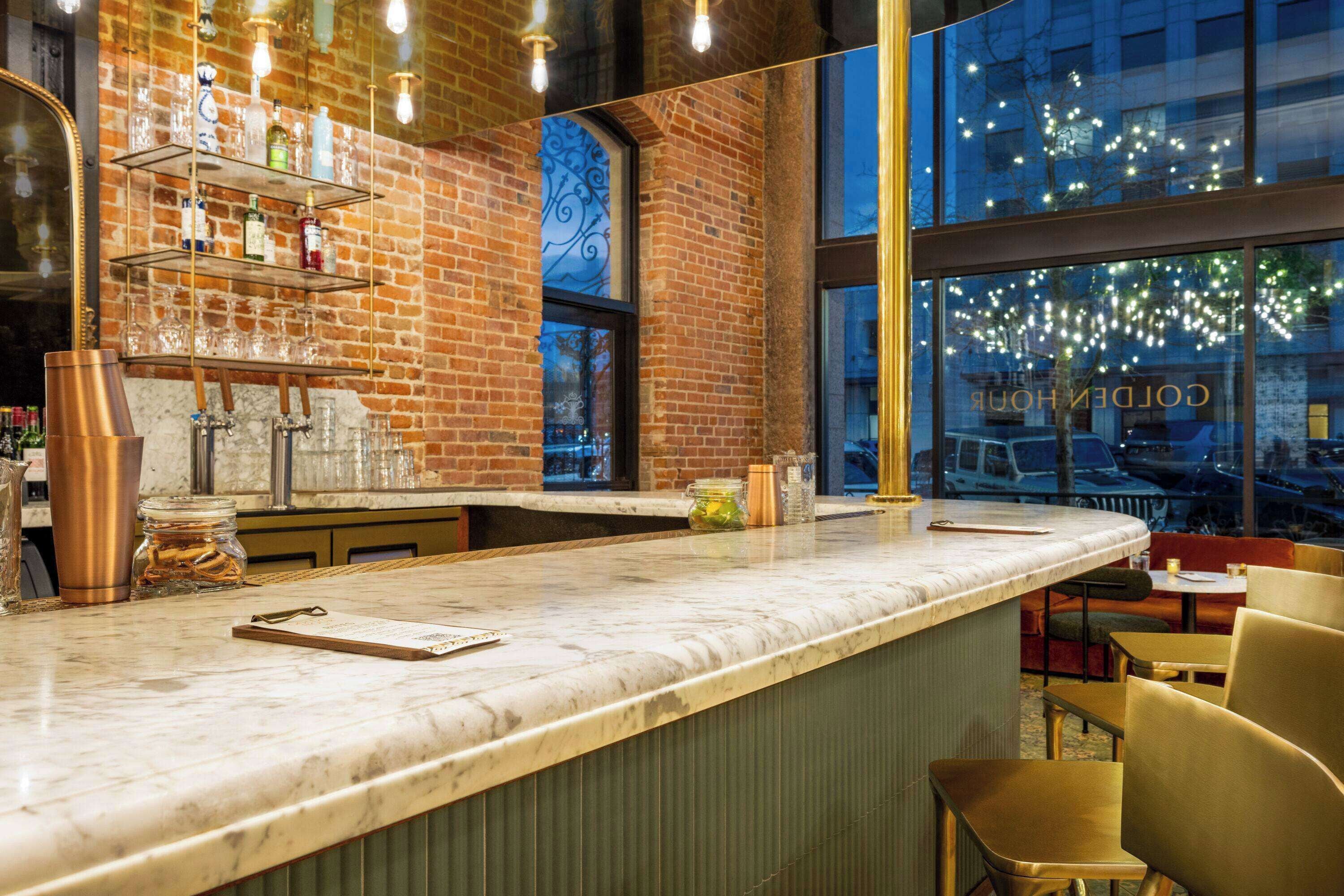 A bar area with a marble countertop, shelves with bottles, and a view of the city through large windows.