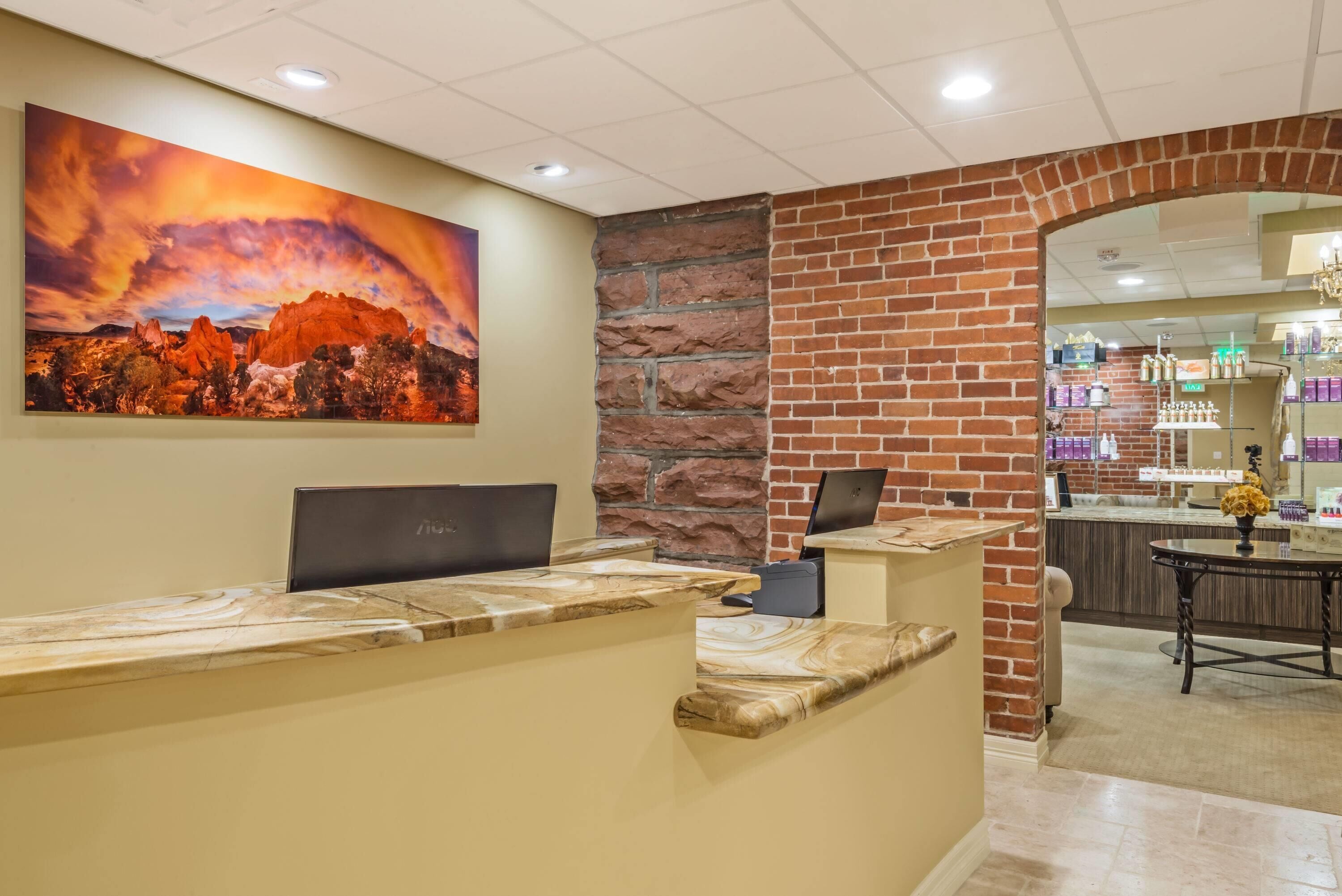 A reception desk with a laptop, a stone wall, and a painting of a landscape.