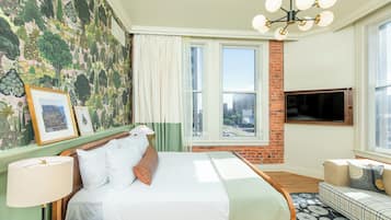 A hotel room with a large bed, a television, a sofa, and a window with a city view.