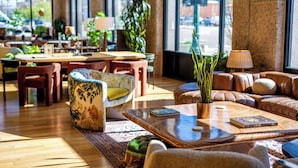 A spacious indoor area with wooden flooring, leather sofas, and a variety of chairs. There are tables with books and a potted plant.