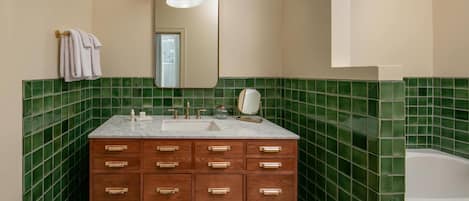 A bathroom with a wooden vanity, a sink, a mirror, and green-tiled walls.