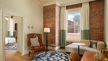 A hotel room with a brick accent wall, a round rug, a sofa, a chair, a small table, and a window with curtains.