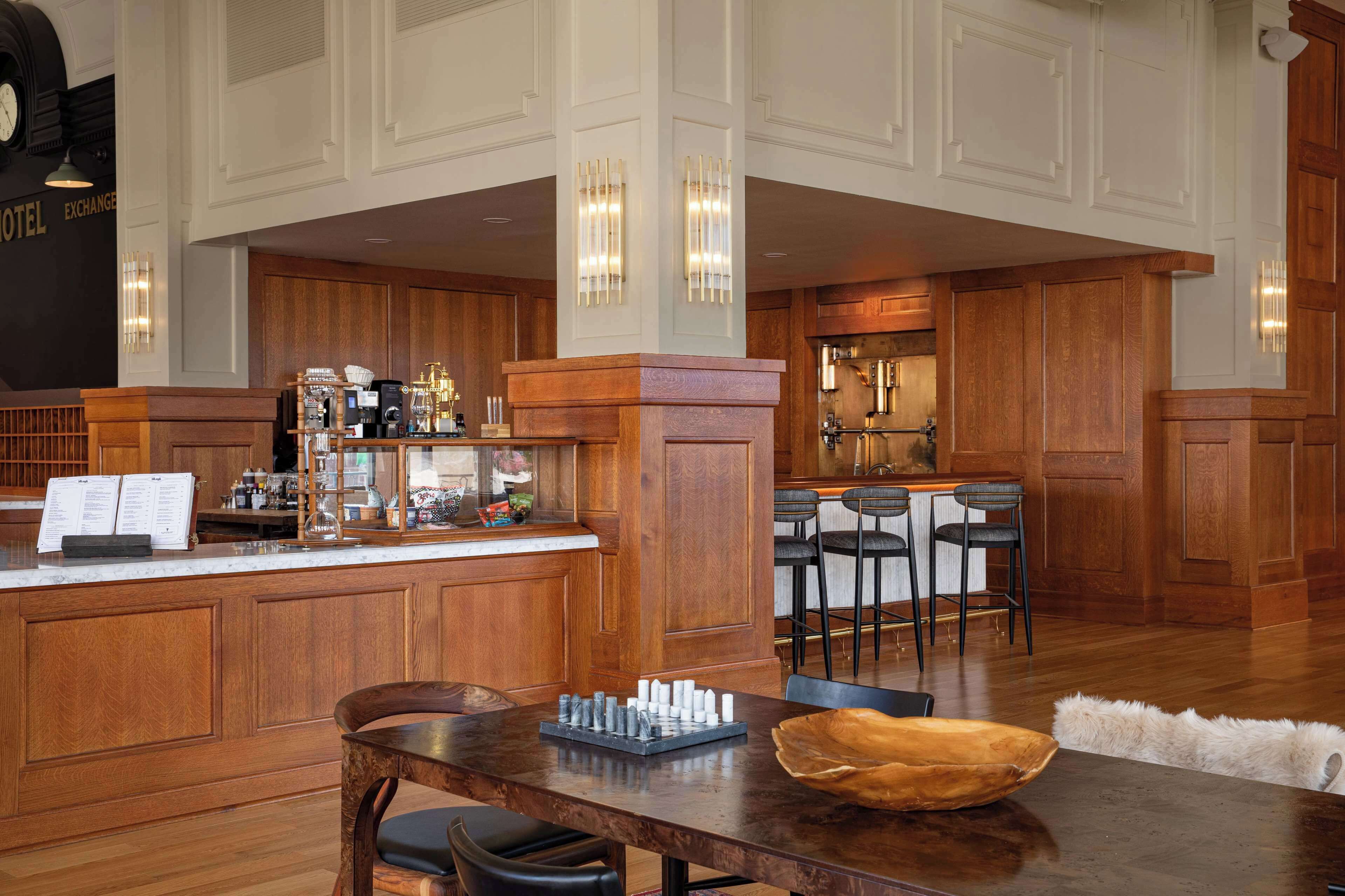 A spacious hotel lobby with a wooden reception desk, bar area, and seating.