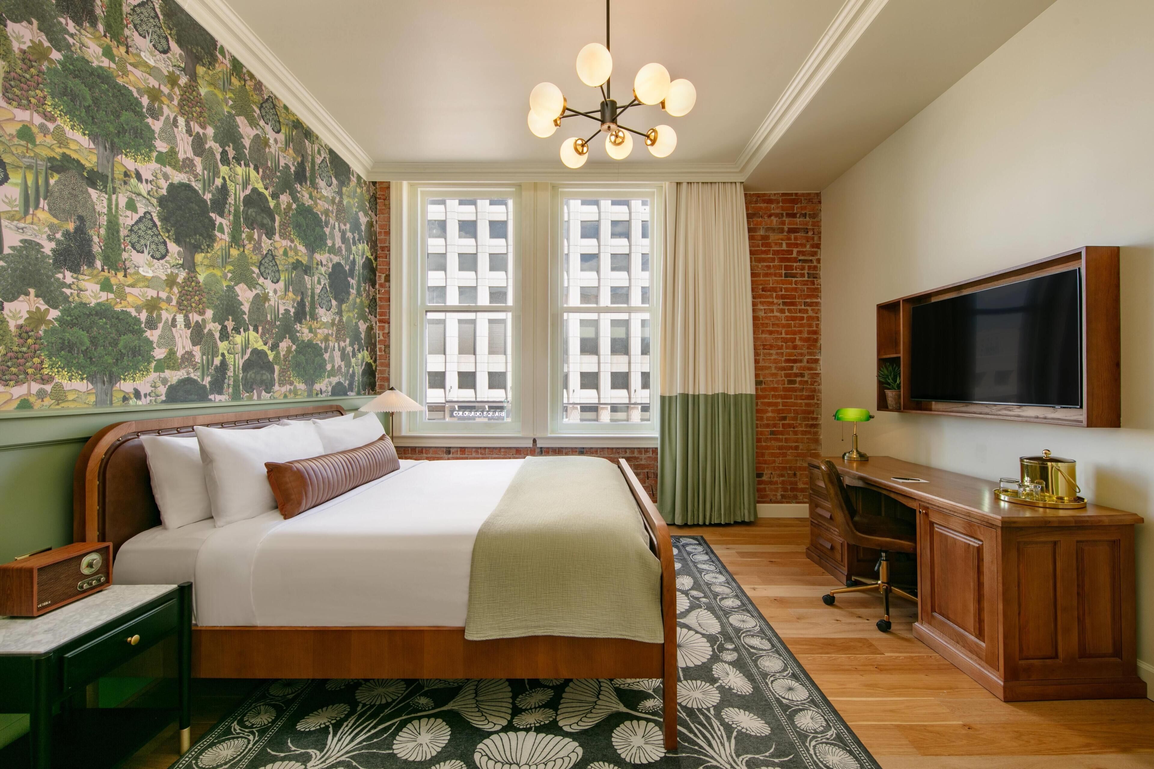 A hotel room with a large bed, a desk, a television, and a mural on the wall.