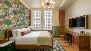 A hotel room with a large bed, a desk, a television, and a mural on the wall.