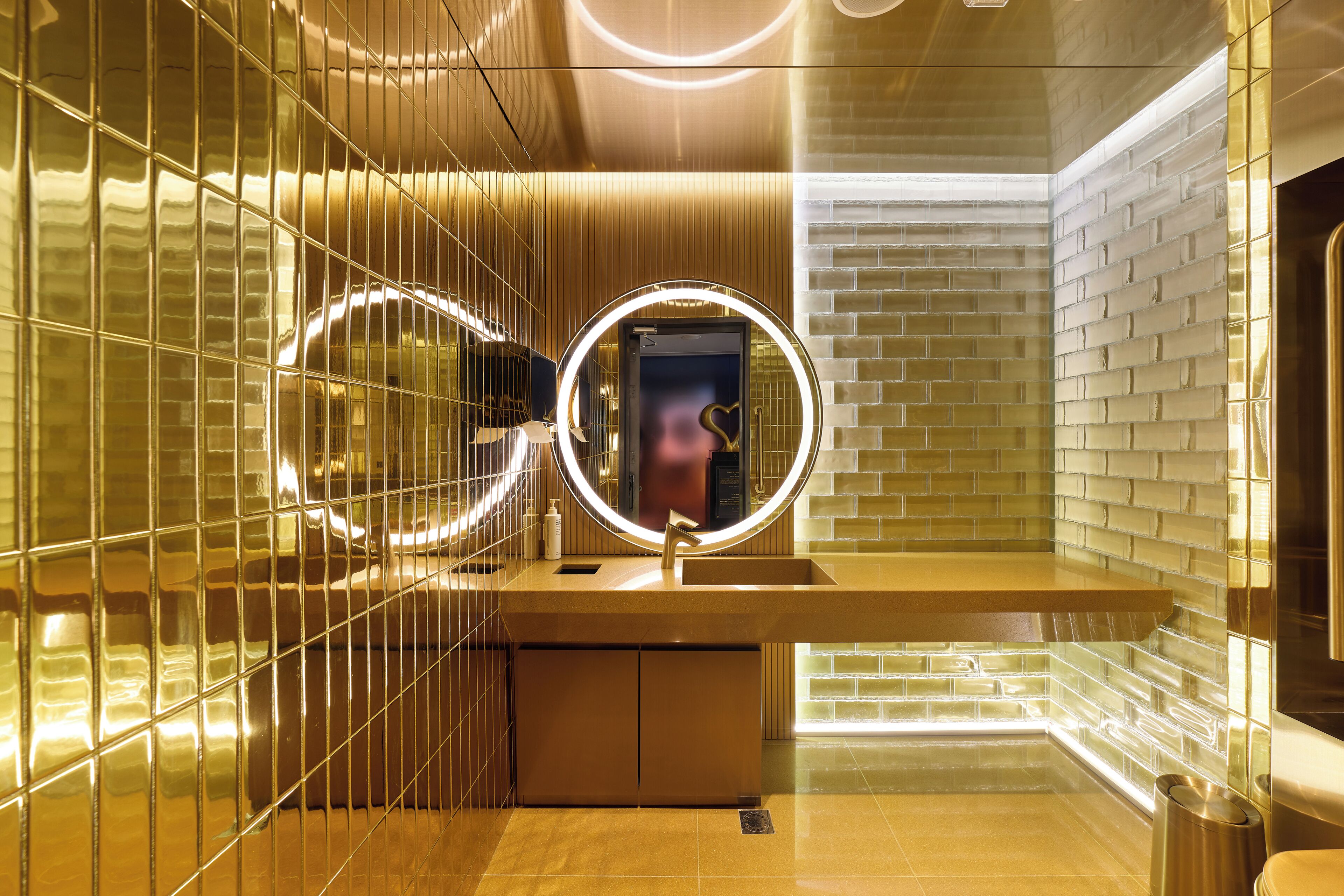 Une salle de bain moderne avec un meuble-lavabo, un miroir doté de lumières disposées en cercle et un mur en briques.