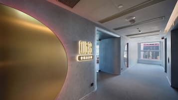 A modern hotel corridor with a curved wall and a neon sign indicating the name and amenities.