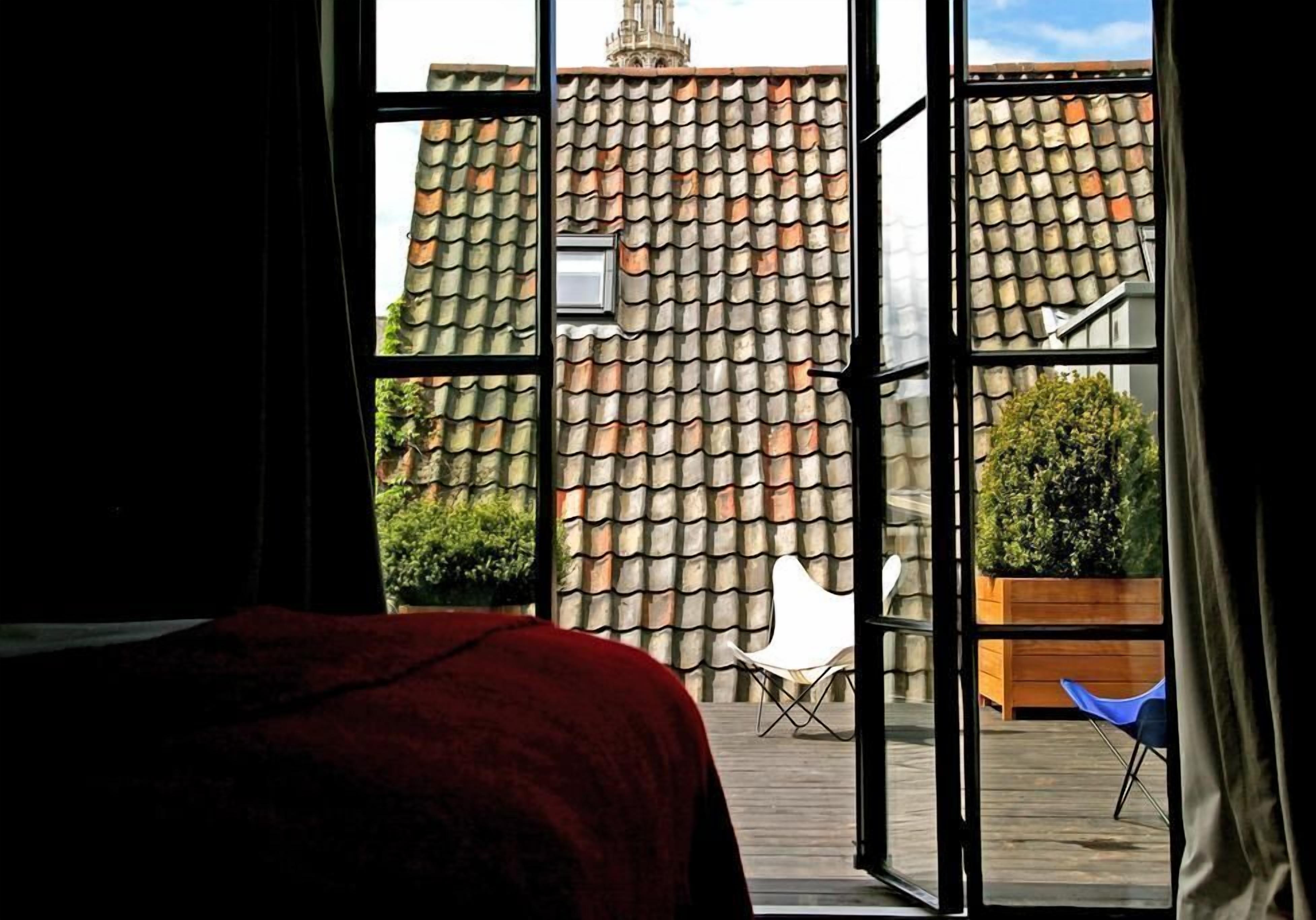 A room with a large window, a bed, and a view of a courtyard with a tiled roof and a chair.