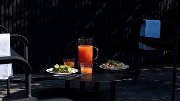 Un espace de restauration en plein air avec une table dressée pour deux personnes, une carafe de thé glacé et une assiette de nourriture.