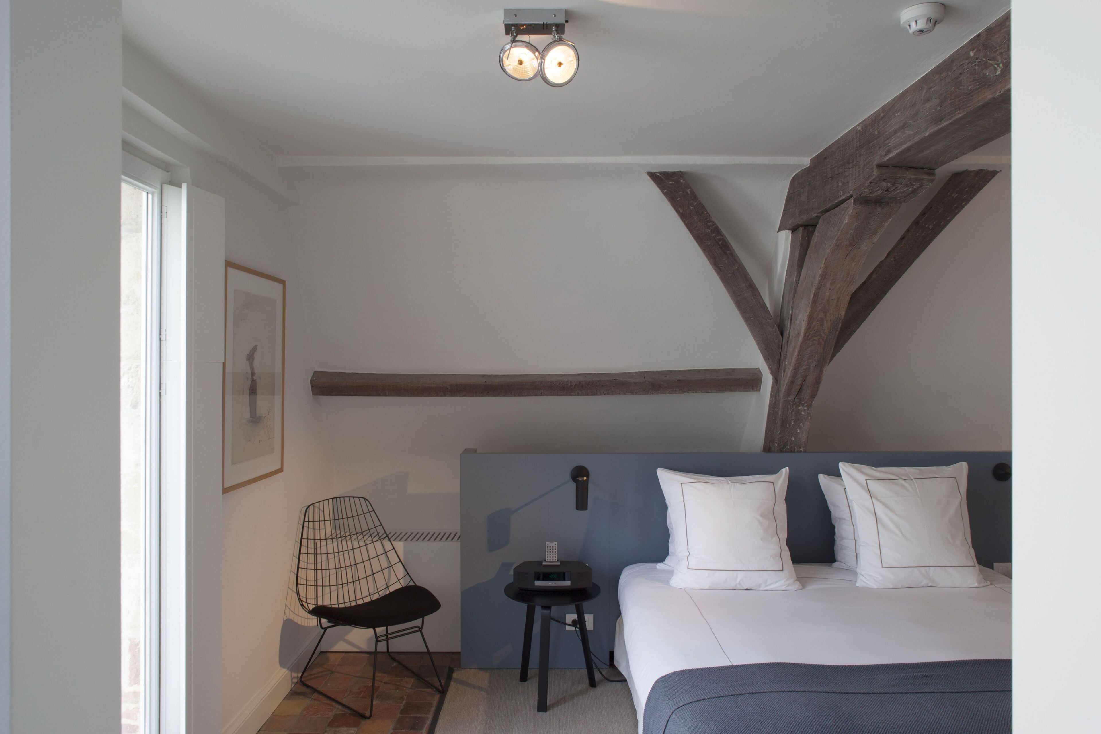 A bedroom with a bed, a chair, a small table, and a ceiling light fixture.