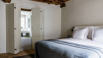 Une chambre à coucher avec un lit, une table de chevet, une commode et une salle de bain visible à travers une porte ouverte.
