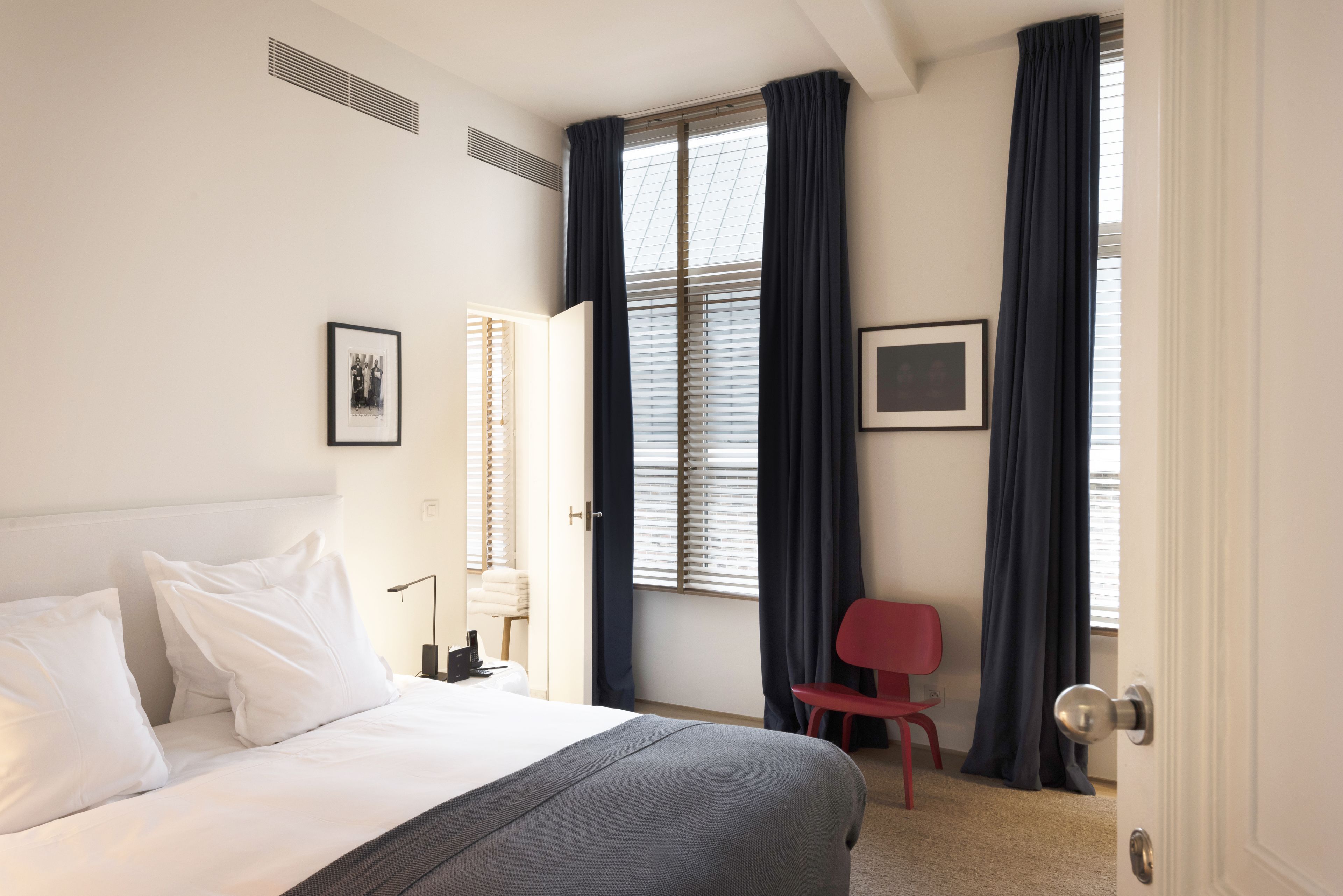 Une chambre d’hôtel avec un lit, une chaise, un bureau et une fenêtre avec des rideaux.