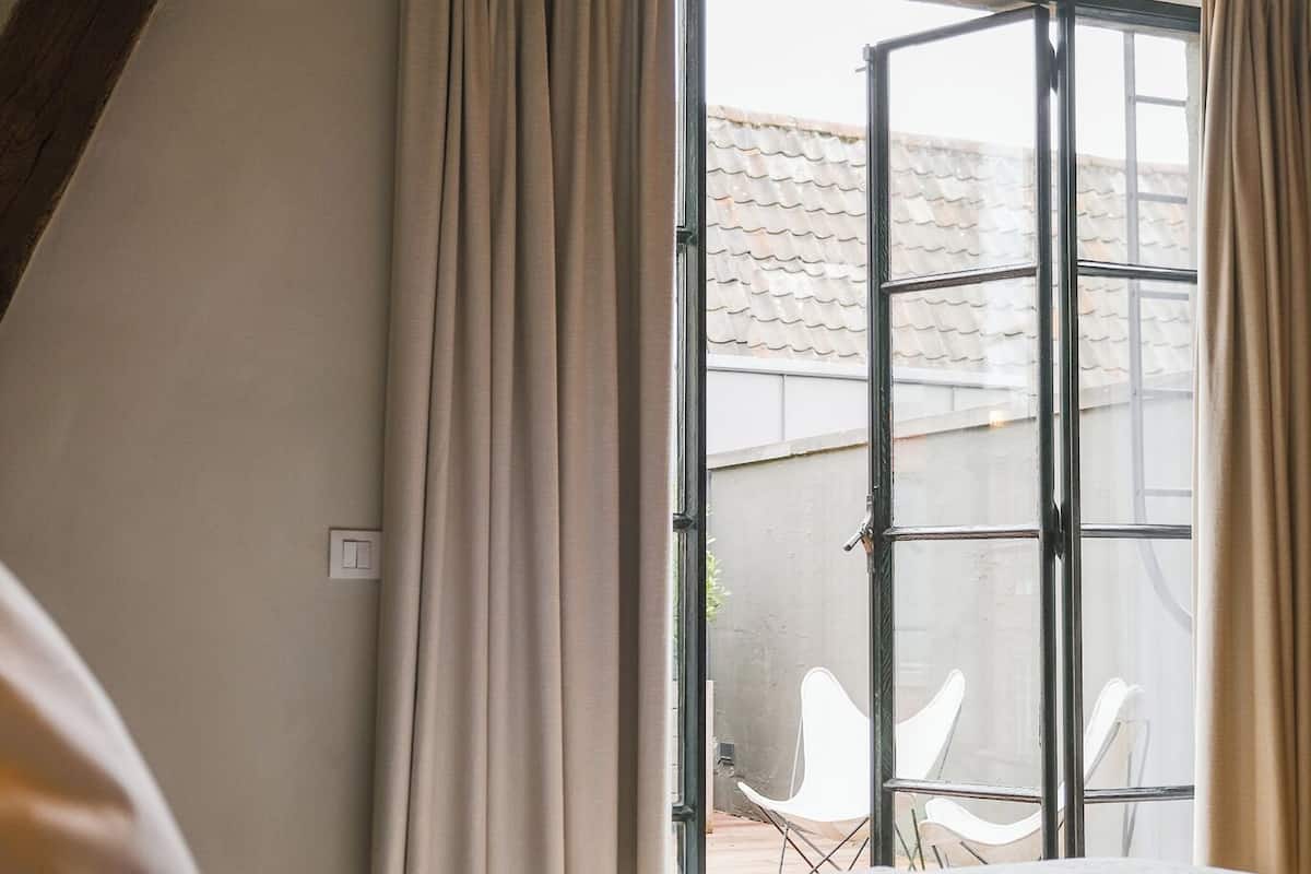 Une chambre avec un grand lit, une fenêtre avec des rideaux et une vue sur des chaises placées à l’extérieur.