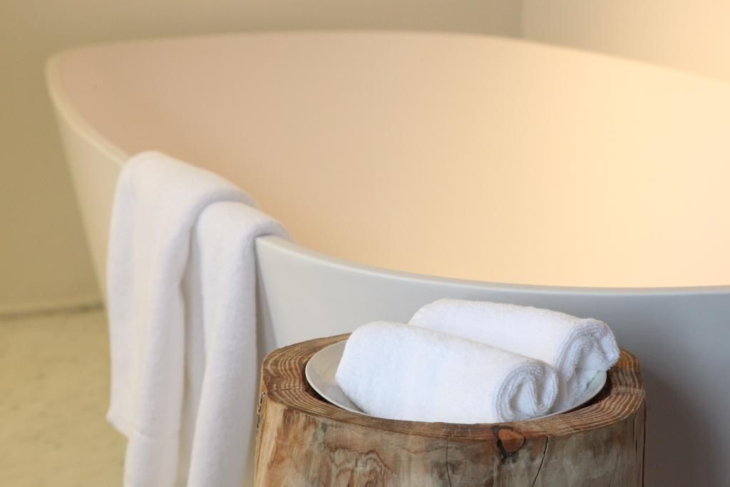 A bathtub with a white towel draped over it and a wooden stool with rolled towels beside it.