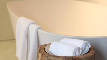 A bathtub with a white towel draped over it and a wooden stool with rolled towels beside it.