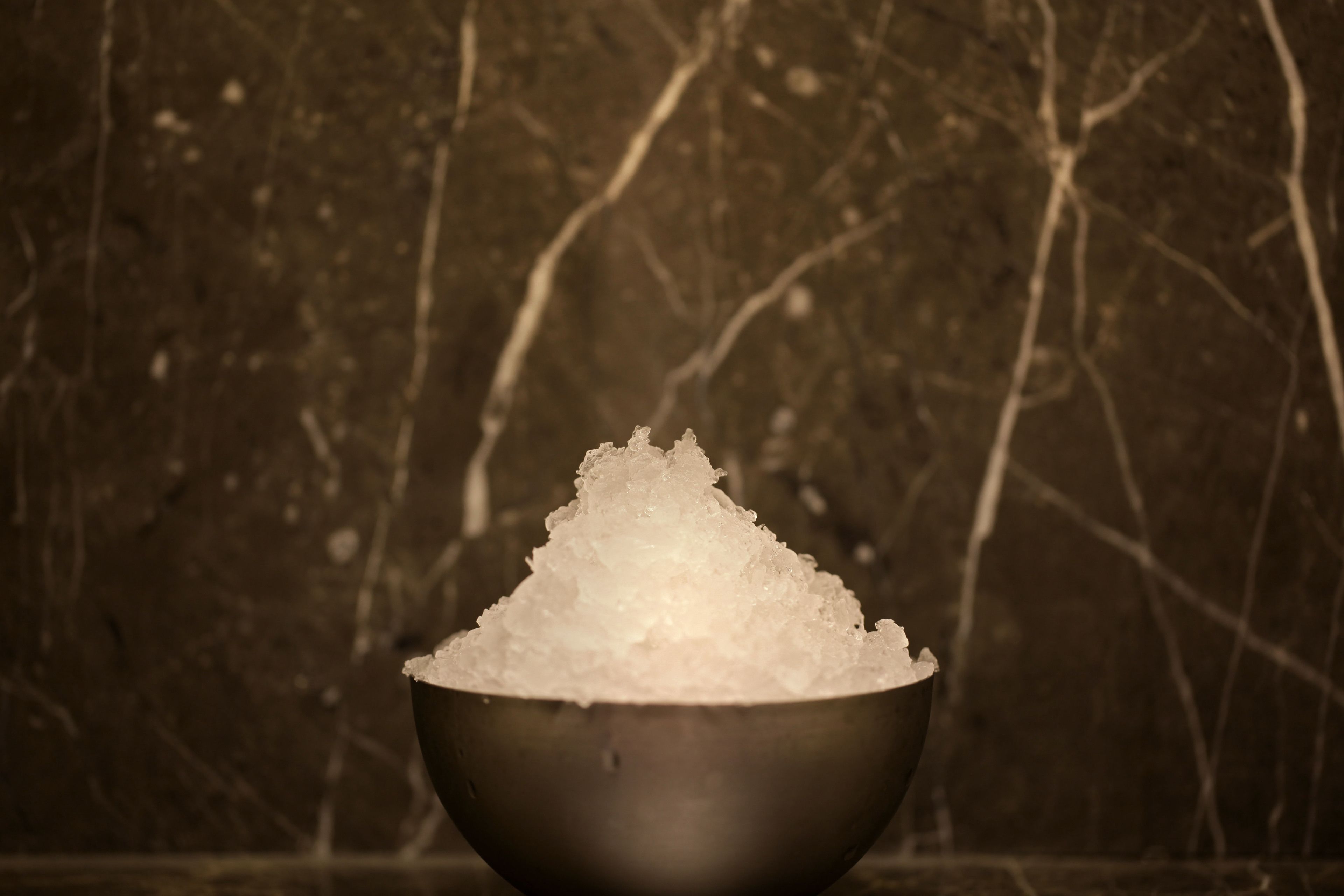 A metallic bowl filled with salt against a textured wall background.