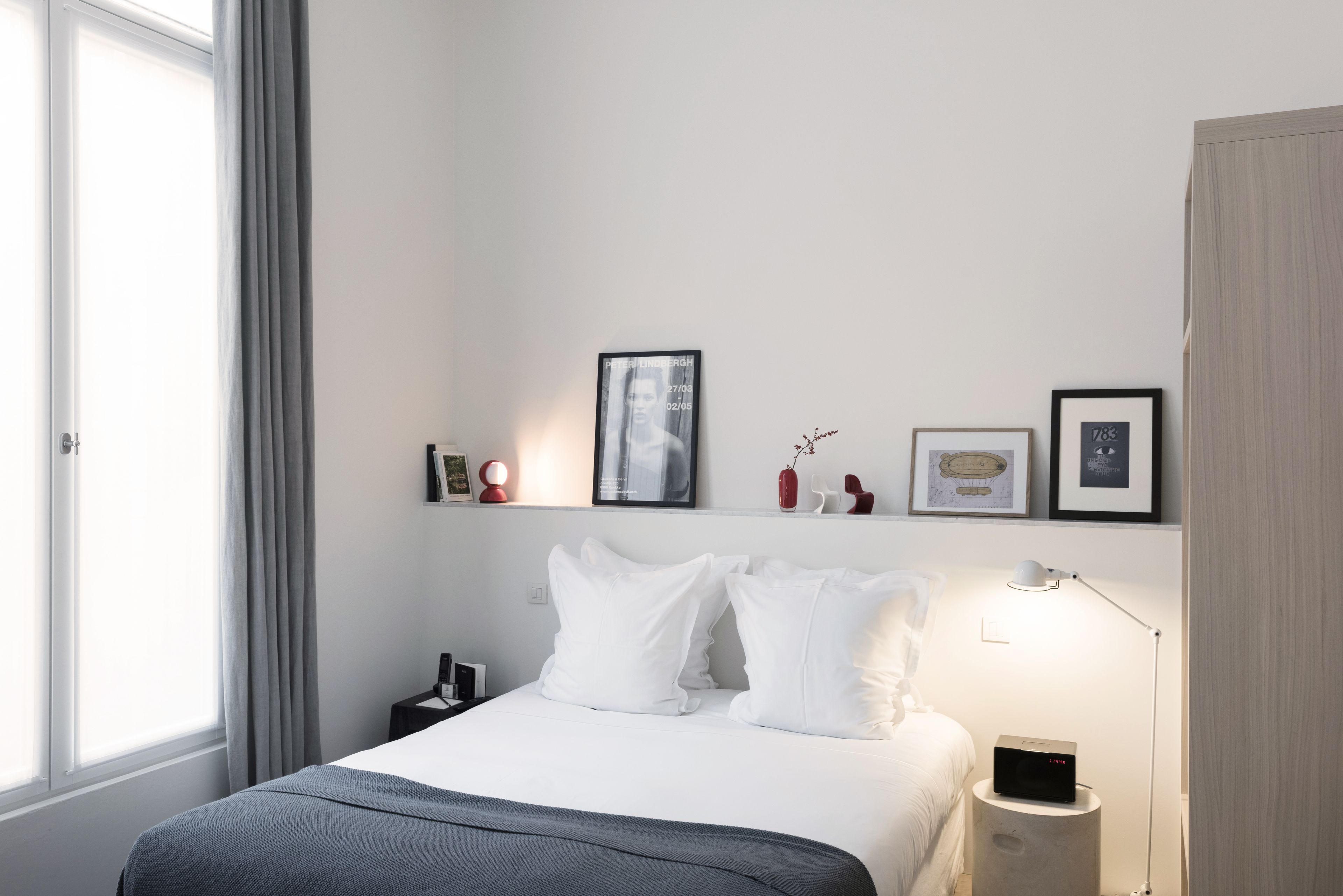 Una habitación de hotel moderna con una cama bien hecha, una mesita de noche con lámpara y una ventana con cortinas.