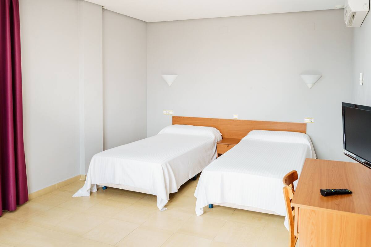 Een hotelkamer met twee eenpersoonsbedden, een houten bureau, een televisie en een rood gordijn.