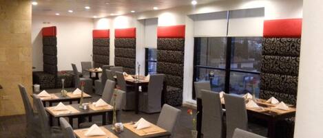 A restaurant with booths and tables, red cushions on the backrests, and a large window with a view.