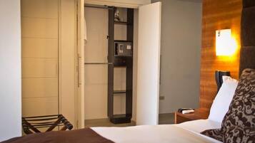 A hotel room with a bed, a nightstand, a chair, a wardrobe, and a wall-mounted light fixture.
