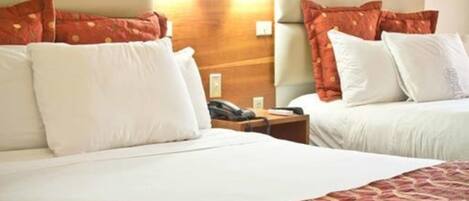 Habitación de hotel con dos camas, cada una con ropa blanca y mantas rojas estampadas. Hay dos mesitas de noche con lámparas, y las paredes están revestidas de madera.