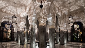 Een statige zaal met versierde zuilen, gedetailleerde plafonddecoraties en hangende lantaarns.