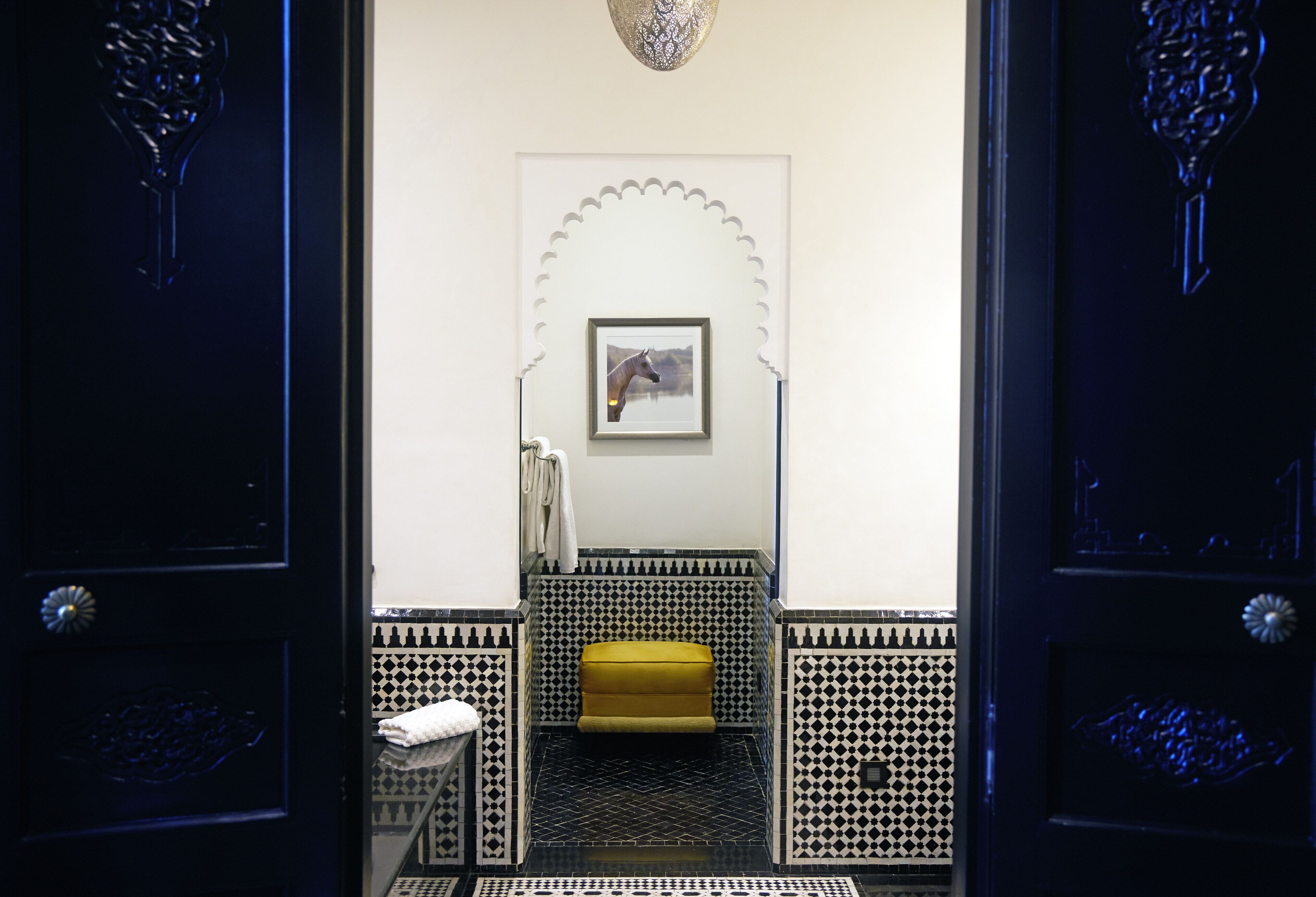 Un baño con piso de estampado blanco y negro, un banco amarillo y un cuadro en la pared.