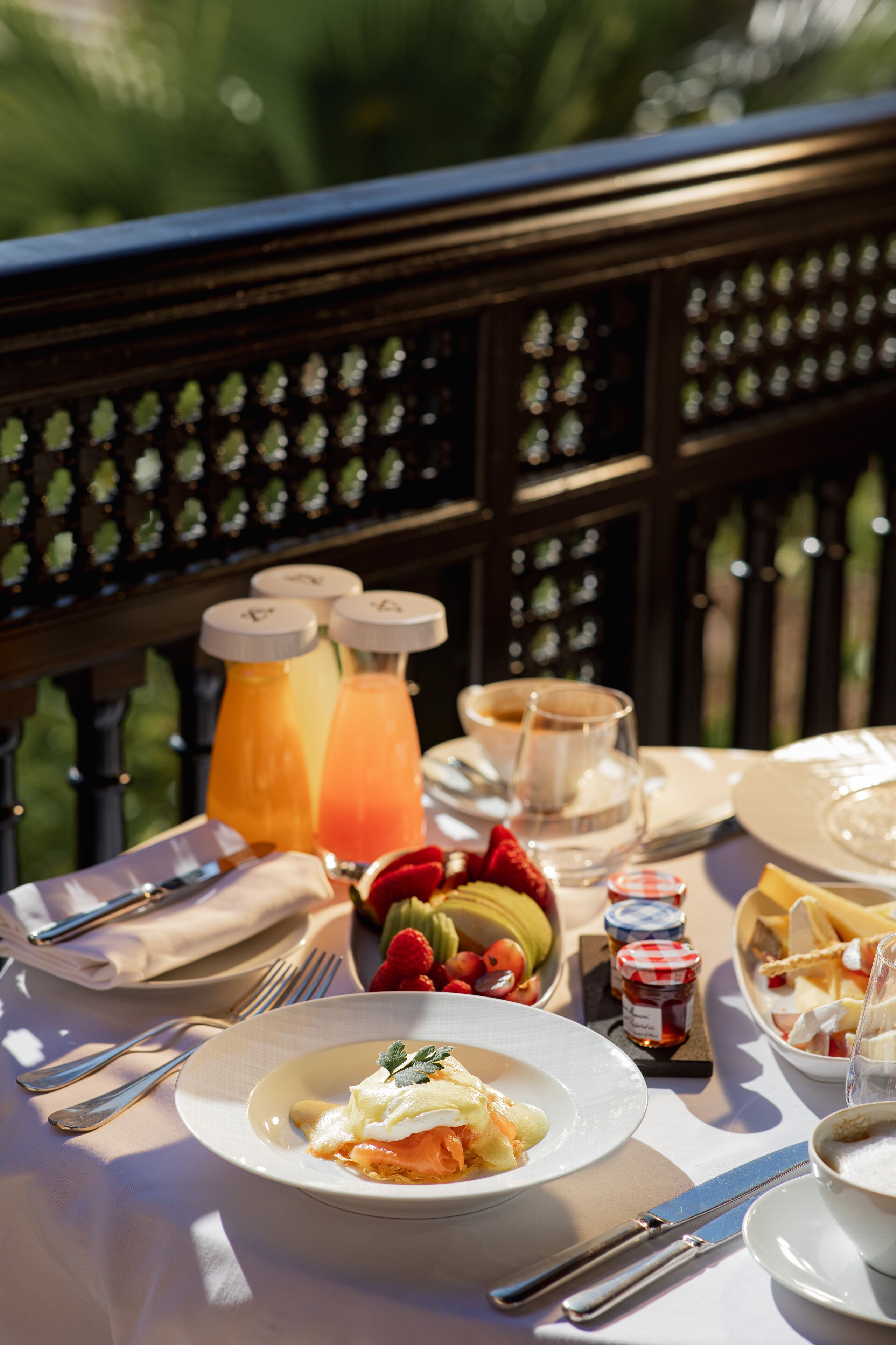 A dining table set outdoors with a variety of food items, including a plate of eggs, a bowl of fruit, and a glass of orange juice.
